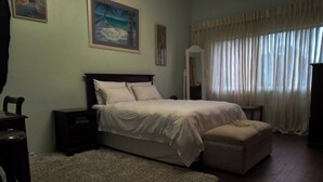 A bedroom with a bed, nightstands, a dresser, a mirror, and a window with curtains.