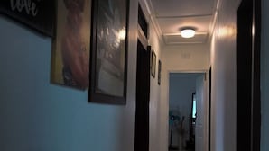 A hallway with framed artwork on the walls, a ceiling light, and a door at the end.