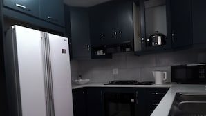 A modern kitchen with dark cabinets, a white refrigerator, a microwave, and a sink.