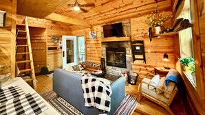 A log cabin interior with a fireplace, a sofa, a ladder, and a television.