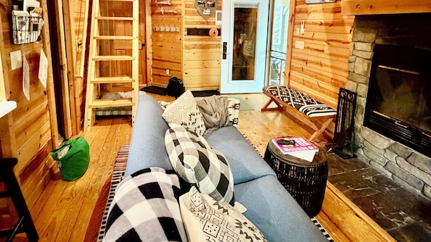 A log cabin interior with a sofa, fireplace, wooden walls, and a ladder.