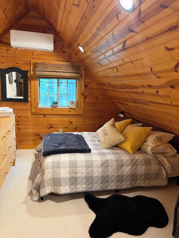 A cozy room with a bed, a dresser, a window with a view, and a ceiling fan.