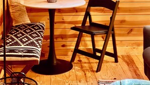 A wooden interior with a round table, two chairs, a small plant, and a banner.