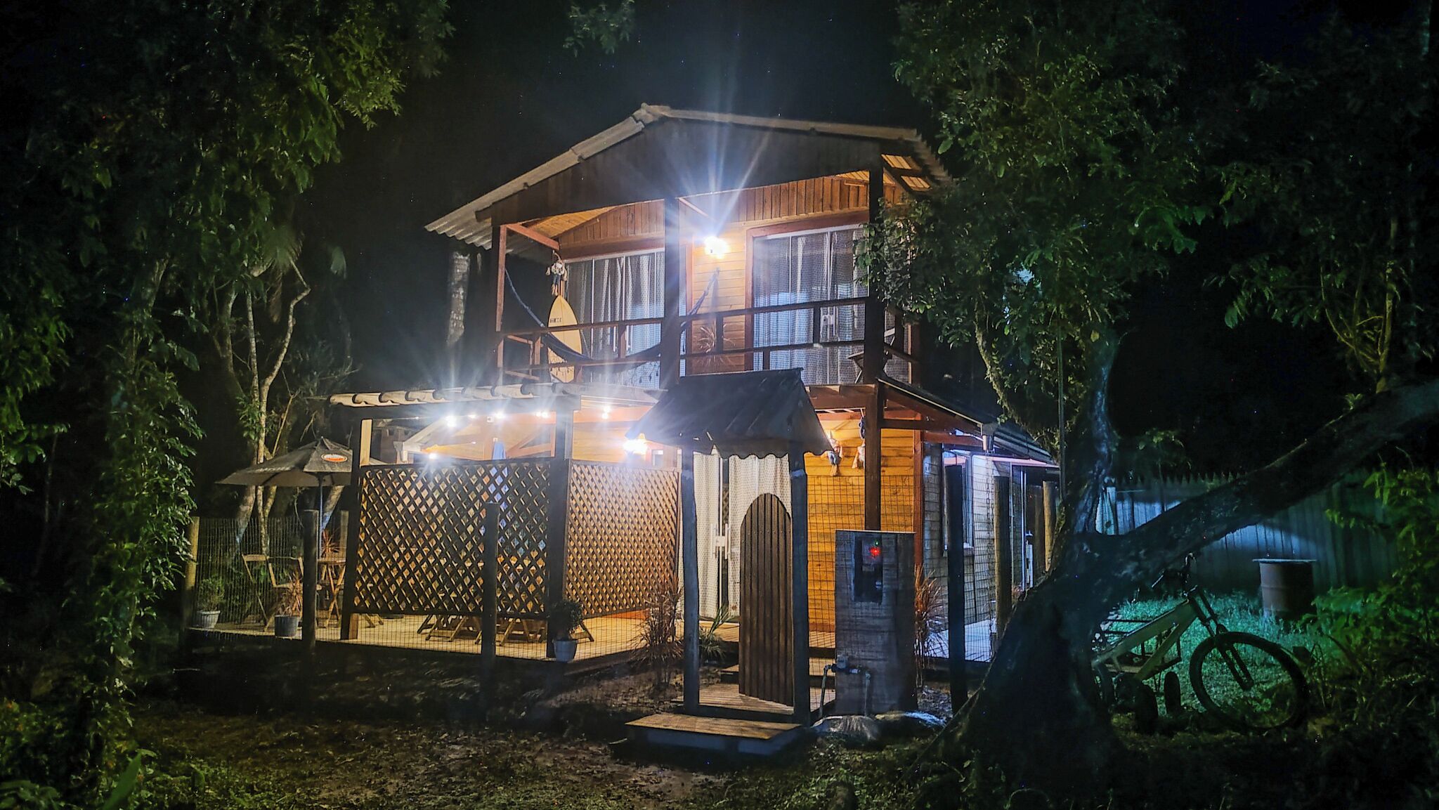 Une maison en bois à deux étages, dotée d’un balcon et entourée d’arbres.