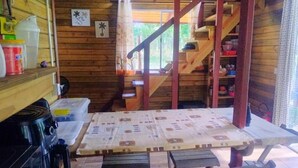 En stuga med träpanel på insidan, innehållande ett köksområde, en trätrappa och ett fönster som släpper in naturligt ljus.