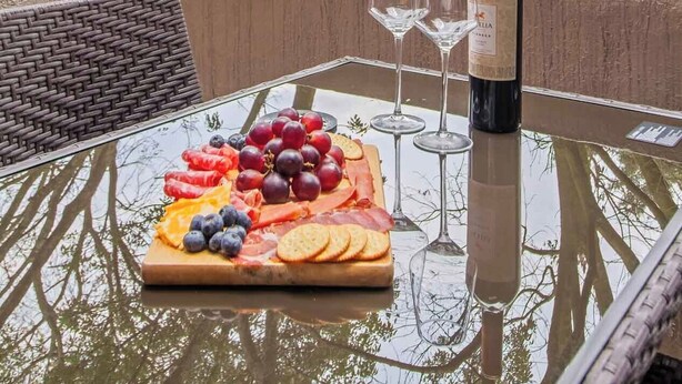A table with a charcuterie board, wine glasses, and a bottle of wine on a balcony with a view of trees and buildings. - Your home with Comfort, Security and BBQ in El Poblado, Medellin! Super location (Medellín)