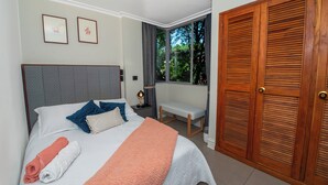 A neatly made bed with pillows and a blanket, a bedside table with a lamp, a bench, and a wooden door. - Your home with Comfort, Security and BBQ in El Poblado, Medellin! Super location (Medellín)