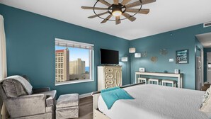 A bedroom with a bed, a reclining chair, a TV, a desk, and a view of a cityscape. - 1BR oceanview studio with private balcony (Miramar Beach)