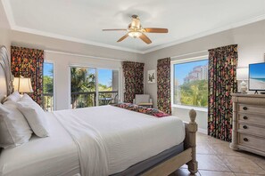 Ein Hotelzimmer mit Bett, Schreibtisch, Stuhl, Deckenventilator und großen Fenstern mit Vorhängen.