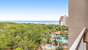 Vista d'un complex turístic amb piscina, envoltat d'arbres i una platja al fons.