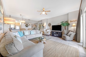 A living room with a sofa, armchair, glass coffee table, and a television. - 3BR condo w/gulf views & resort pools (Miramar Beach)