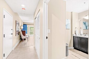A hallway leading to a bathroom with a sink, mirror, and towel rack. - 1BR condo steps to beach, pools, hot tub (Miramar Beach)