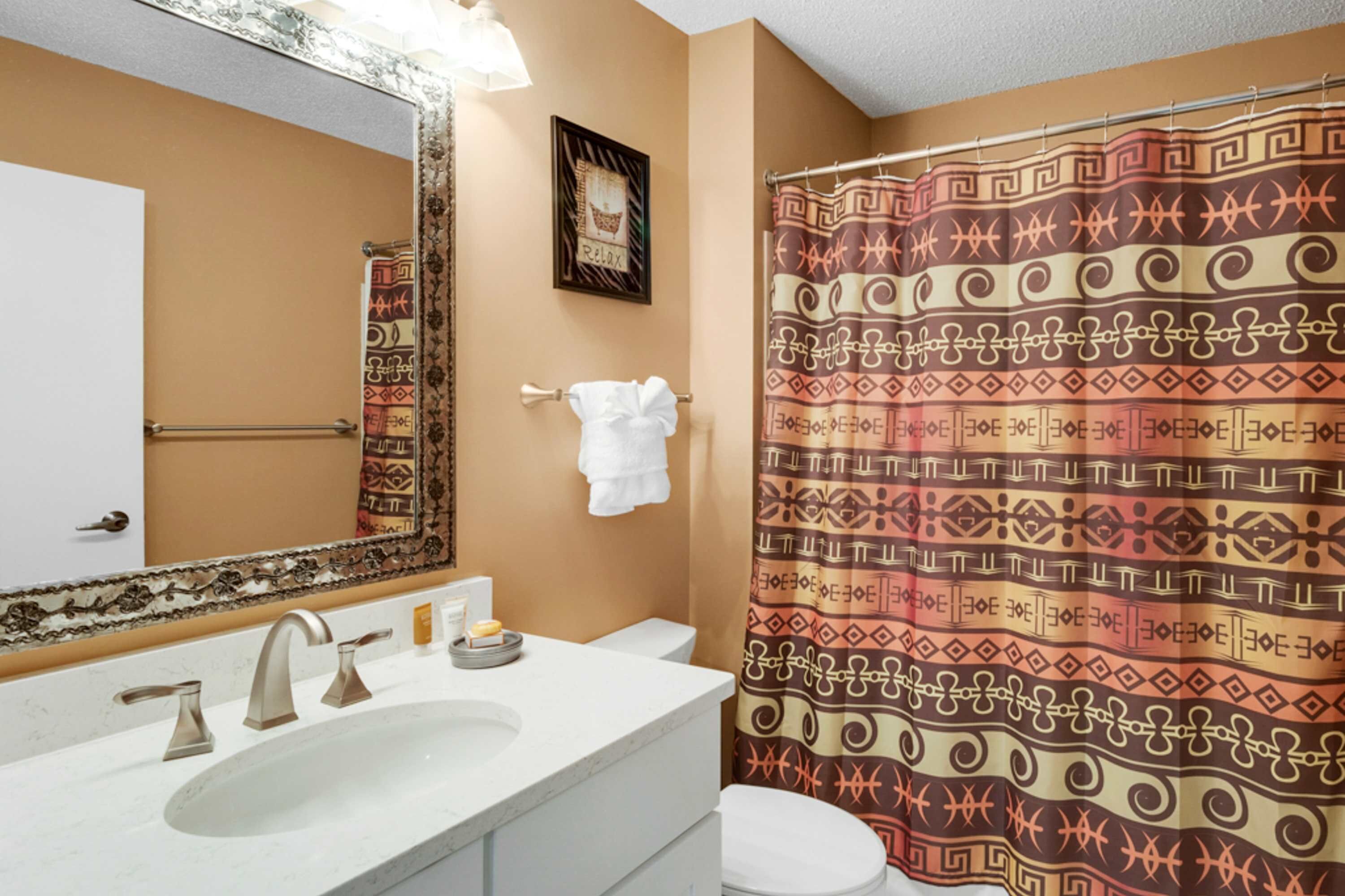A bathroom with a sink, mirror, towel rack, and patterned shower curtain.