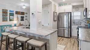 Una cocina moderna con una isla central, electrodomésticos de acero inoxidable y una pared decorativa con letreros de temática náutica.
