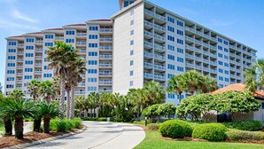 Un hotel de varios pisos con balcones, rodeado de palmeras y jardines cuidados.