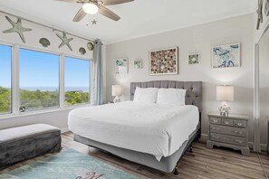 Een slaapkamer met een groot bed, een nachtkastje, een bankje, decoratie aan de muur in de vorm van zeesterren, en uitzicht op de oceaan.