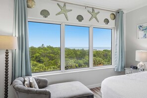 A bedroom with a large window, a gray armchair, a white bed, and a nightstand with a lamp. - Exclusive 3BR with Gulf views, sleeps 8 (Miramar Beach)
