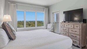 Quarto de hotel com uma cama grande, televisão, ventoinha no teto e vista para o exterior.