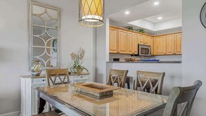 Uma área de refeições com mesa de vidro, cadeiras de madeira, um cesto decorativo e um lustre.