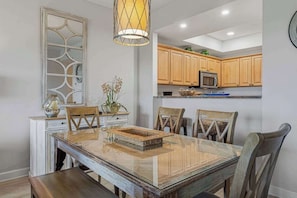 A dining area with a glass table, wooden chairs, a decorative basket, and a hanging light fixture. - Exclusive 2BR: ocean views, pool, hot tub (Miramar Beach)