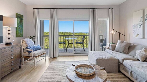 Quarto moderno com sofá, poltrona, mesa de jantar e varanda com vista.