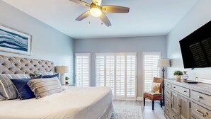 A bedroom with a large bed, a ceiling fan, a dresser, and a television. - Exclusive Studio: Balcony, Pool, Beach Access (Miramar Beach)
