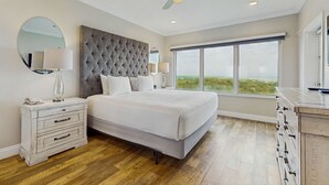 Ein Schlafzimmer mit einem großen Bett, einem Nachttisch, einer Kommode, einem Deckenventilator und einem großen Fenster.