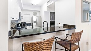 A modern kitchen with a glass island, stainless steel appliances, and wicker chairs. - Steps to beach, ocean views, pool access (Miramar Beach)