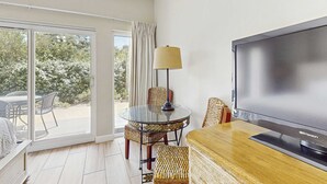 Ett rum med en tv, ett glasbord, flätade stolar och utsikt genom en skjutdörr.