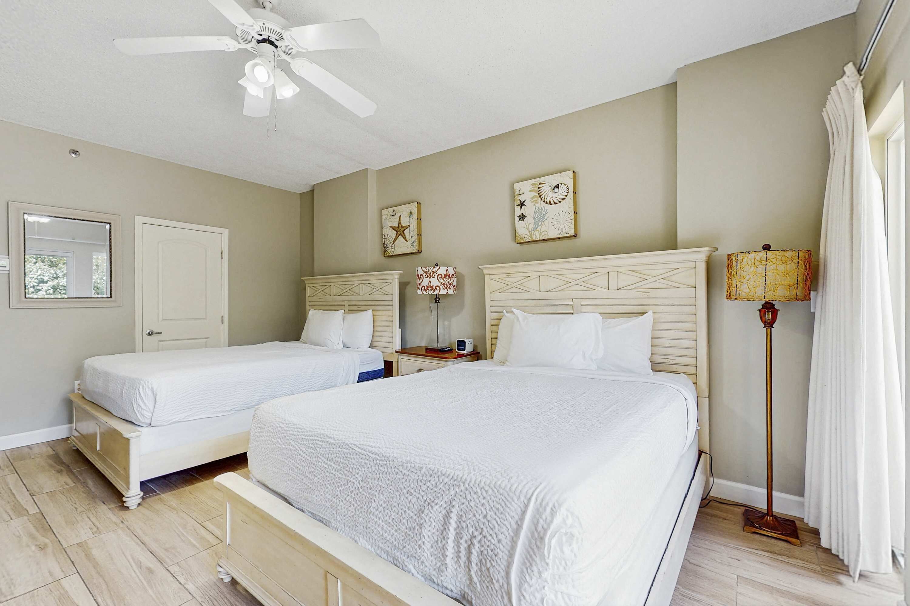 Une chambre d’hôtel avec deux lits, un ventilateur de plafond, une table de chevet avec une lampe et une horloge murale.