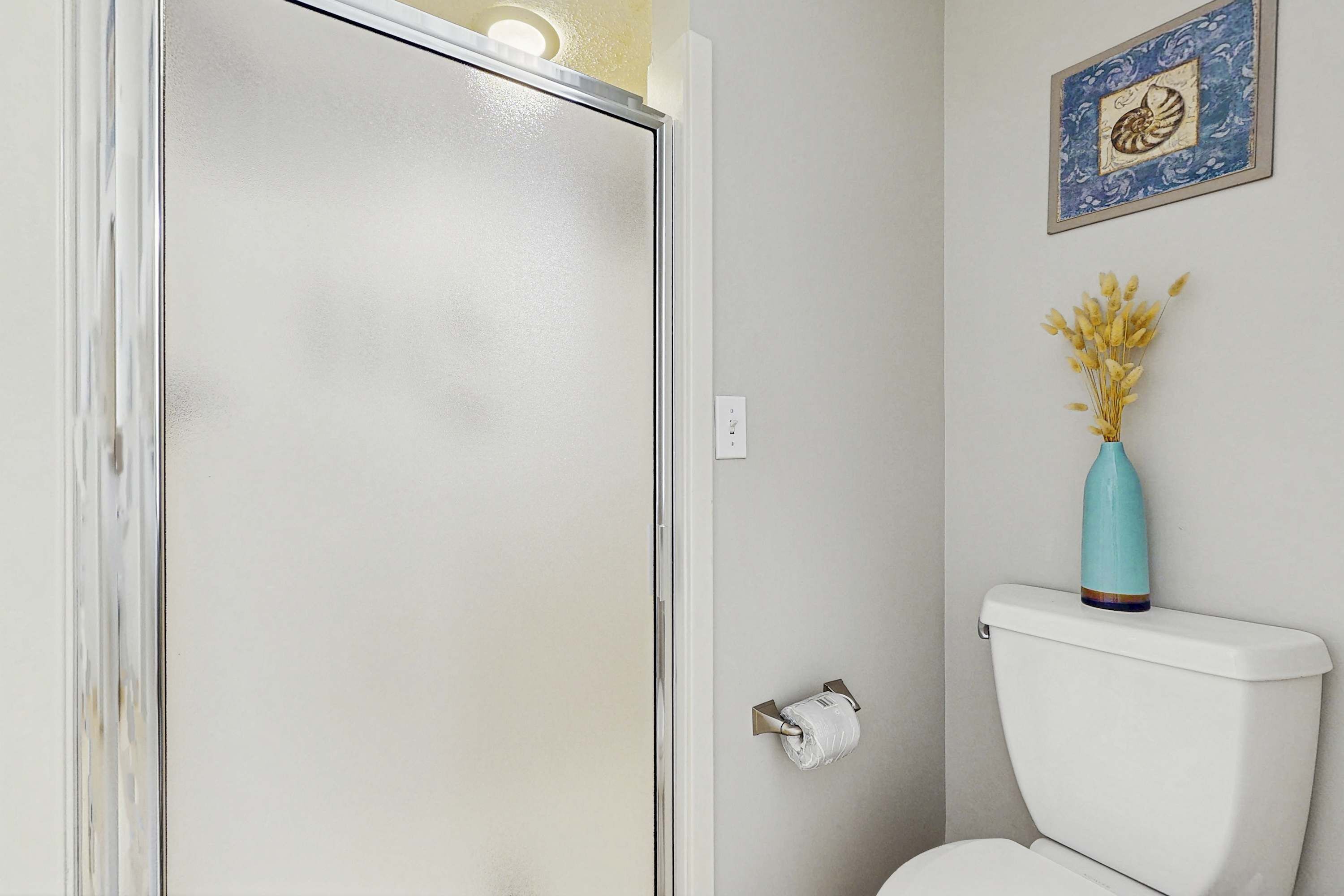 A bathroom with a toilet, a towel rack, and a vase with dried flowers on the wall.