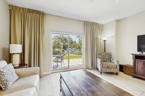 A living room with a sofa, armchair, and a TV stand. - 2BR Resort Condo: Beach Access & Pools (Miramar Beach)