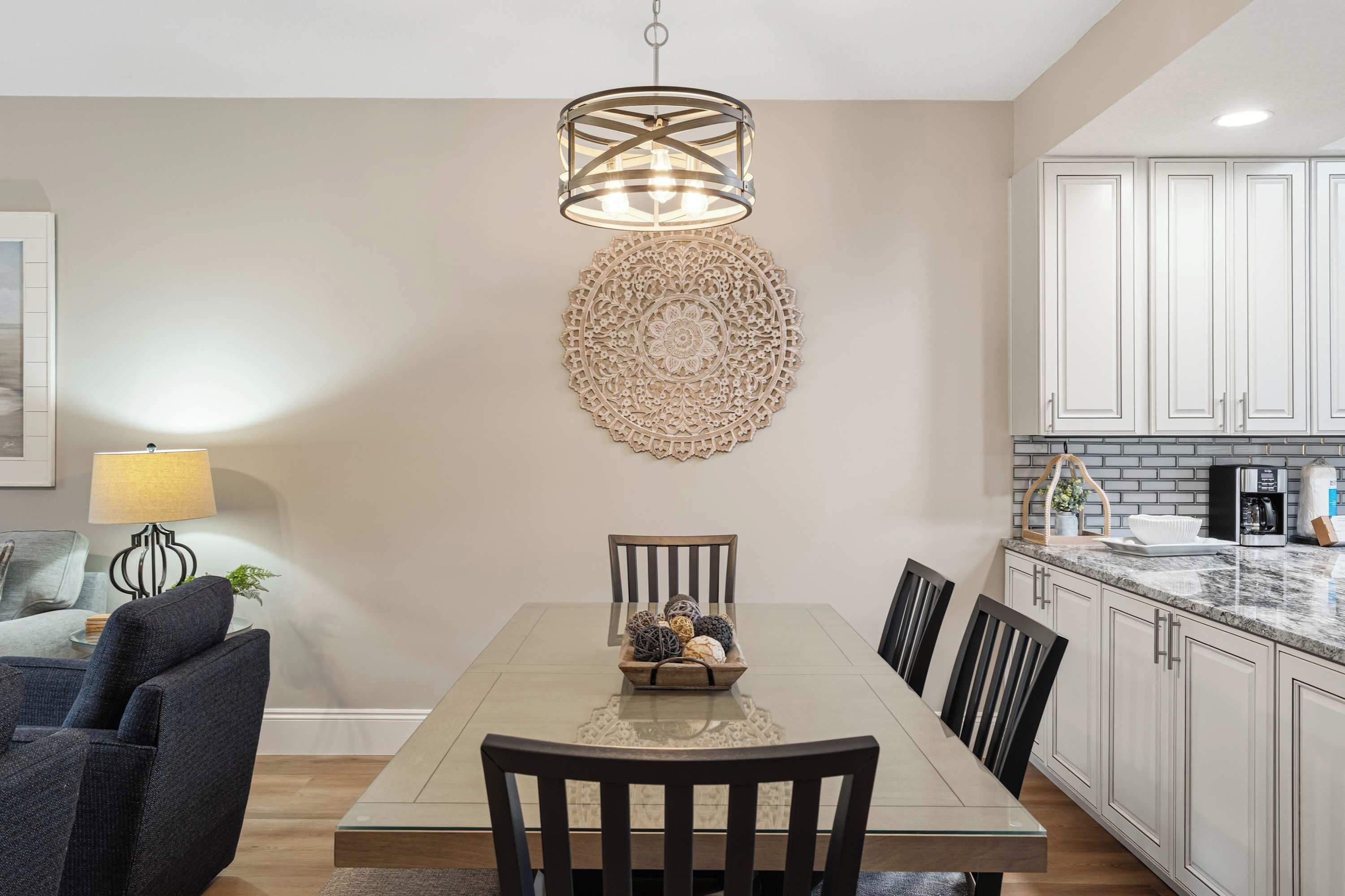 A dining area with a table, chairs, a decorative wall piece, and a kitchen with cabinets and appliances.