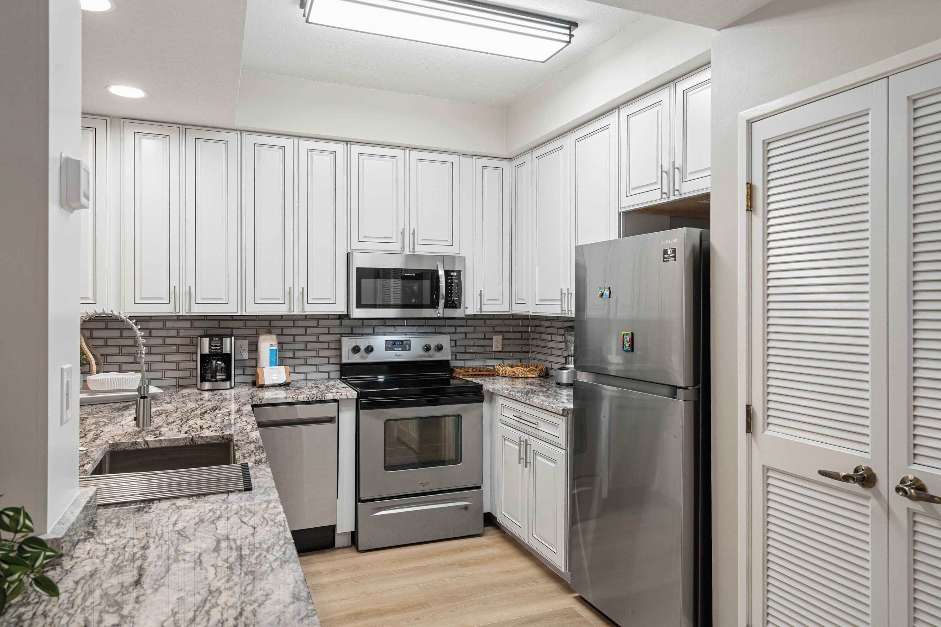 A modern kitchen with white cabinets, stainless steel appliances, and a marble countertop.