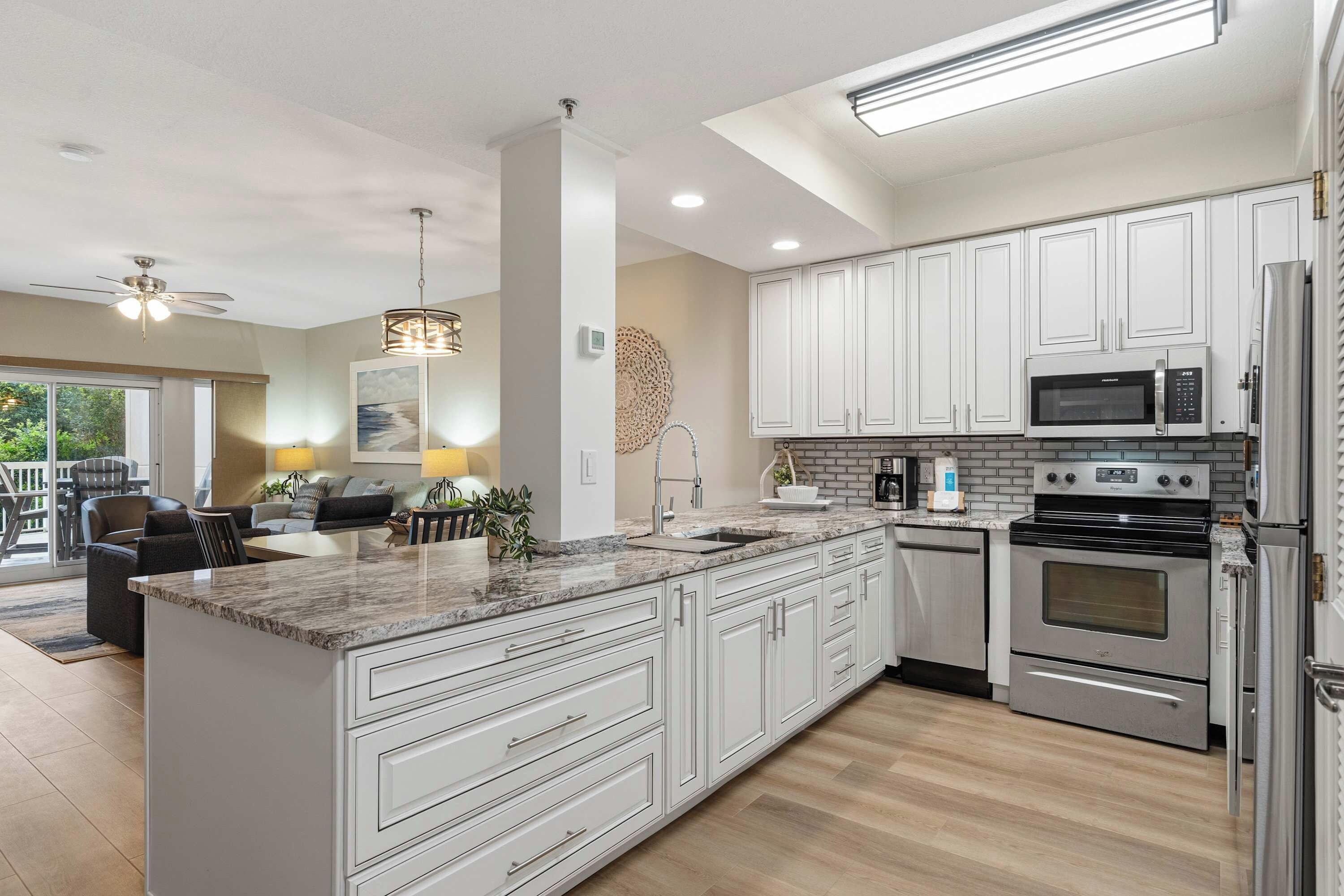 A modern kitchen with white cabinetry, a central island, stainless steel appliances, and a dining area with a view.