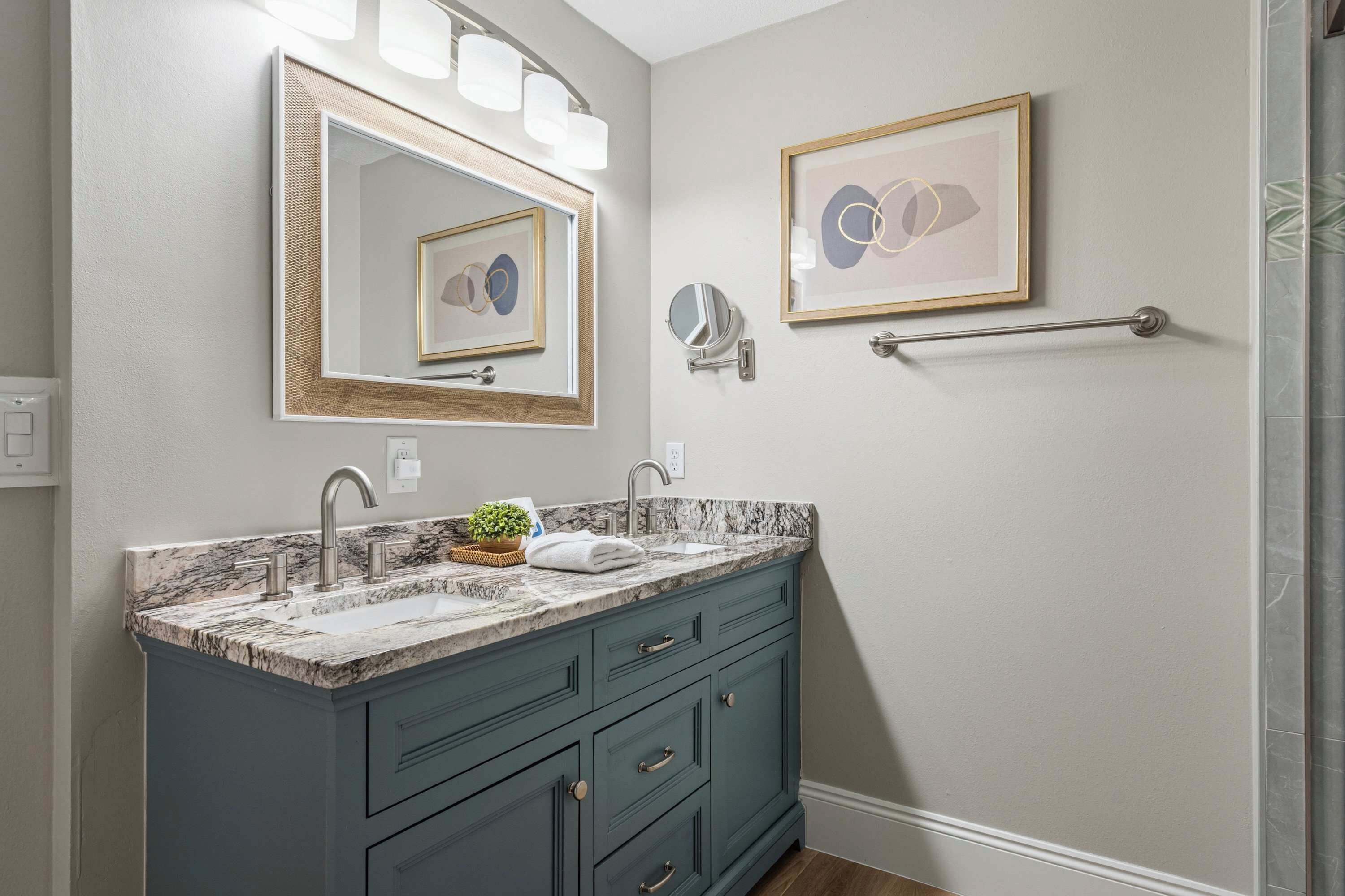 A bathroom with a marble sink, a towel, a mirror with lights, and two framed pictures on the wall.