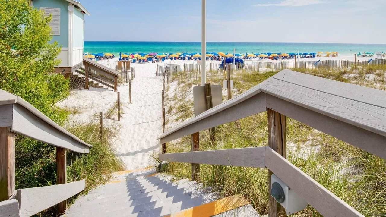 A wooden staircase leading to a beach area with a lifeguard tower and beach umbrellas.
