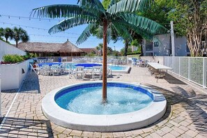 Área de piscina com espreguiçadeiras, uma banheira de hidromassagem e uma palmeira.