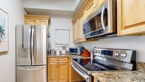 A kitchen with stainless steel appliances, wooden cabinets, granite countertops, and a microwave. - 2BR condo with pool view & private balcony (Miramar Beach)