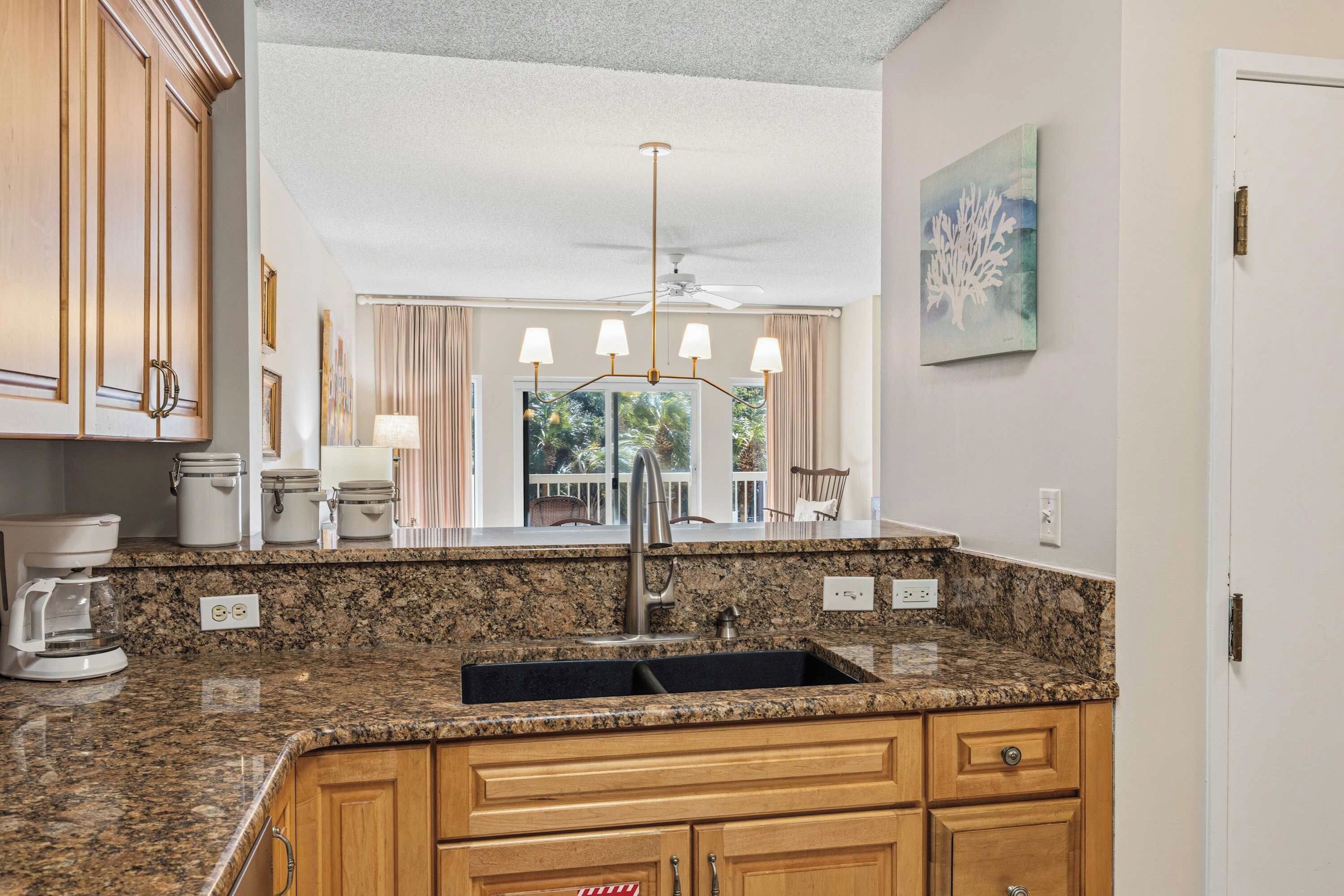 A kitchen with granite countertops, a sink, wooden cabinets, a ceiling fan, and a view of the outdoors.
