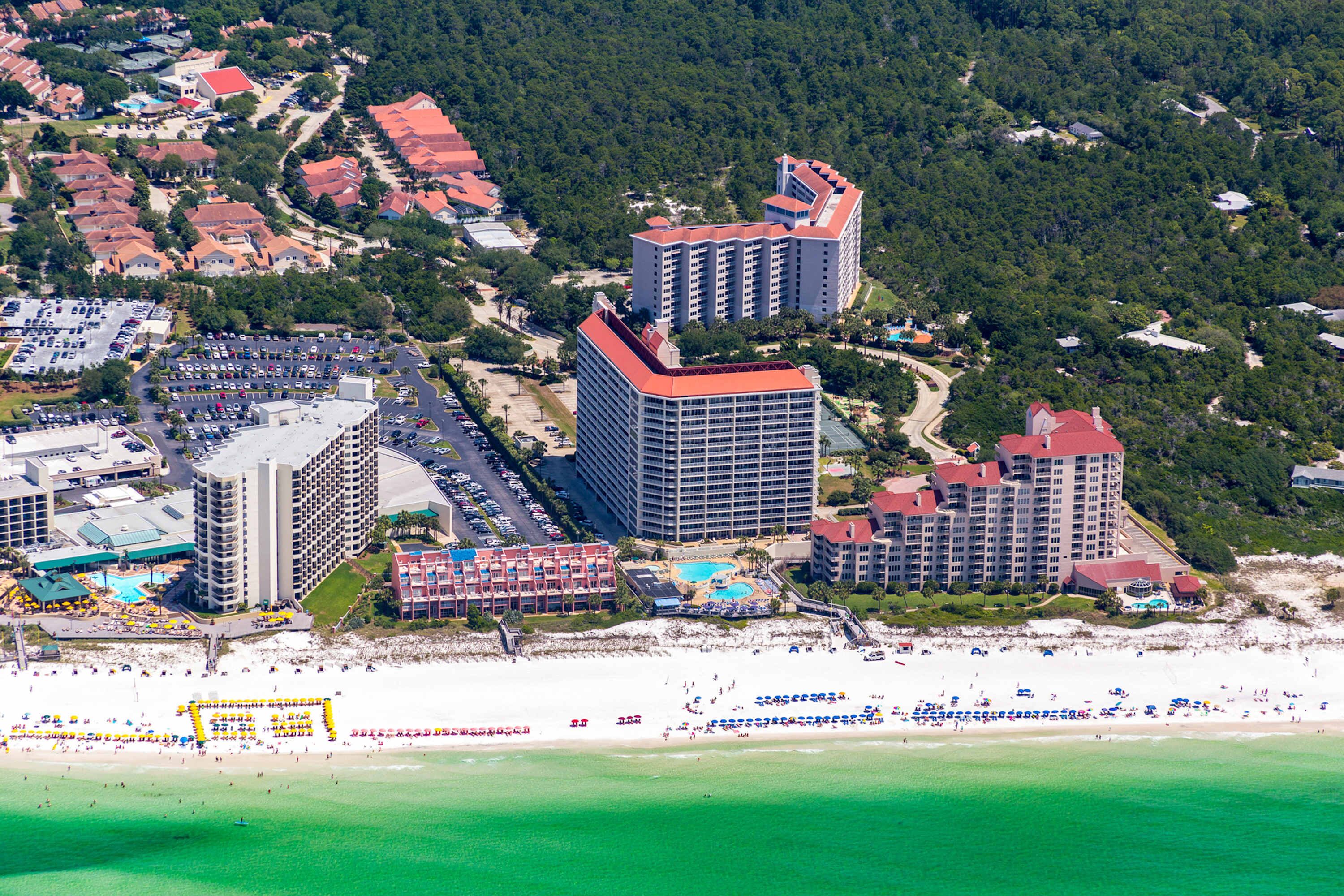 A coastal hotel with multiple high-rise buildings, a beach, and a parking lot.