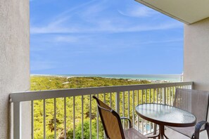 A balcony with a table and chairs, overlooking a coastal landscape with greenery and a view of the sea. - 1BR retreat: hot tub, steps to beach access (Miramar Beach)