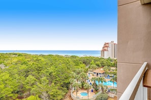 Une vue d’un hôtel avec une piscine, entouré de verdure et surplombé d’un ciel bleu clair.