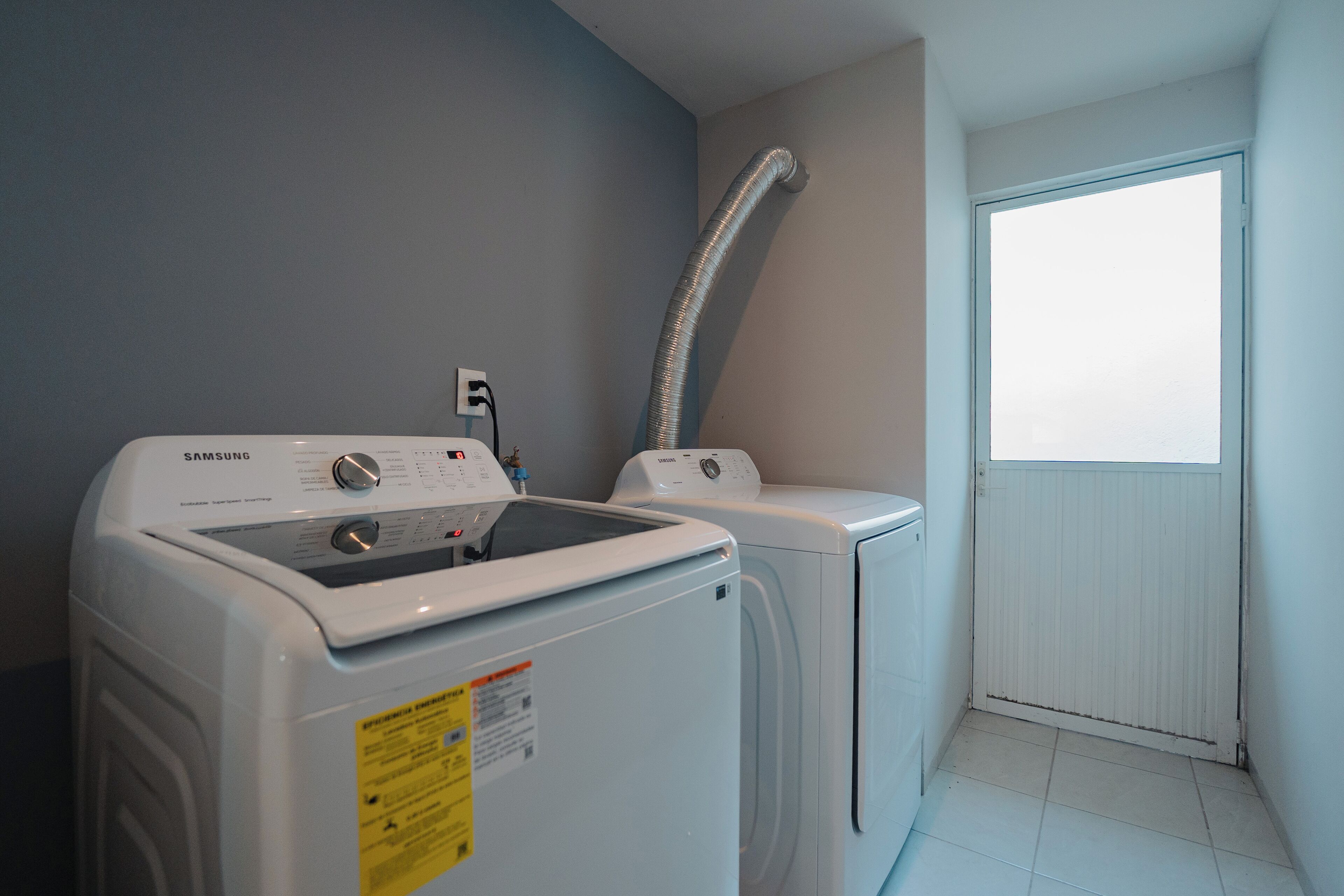 A laundry room with a Samsung washer and dryer, a vent hose, and a window with a view.