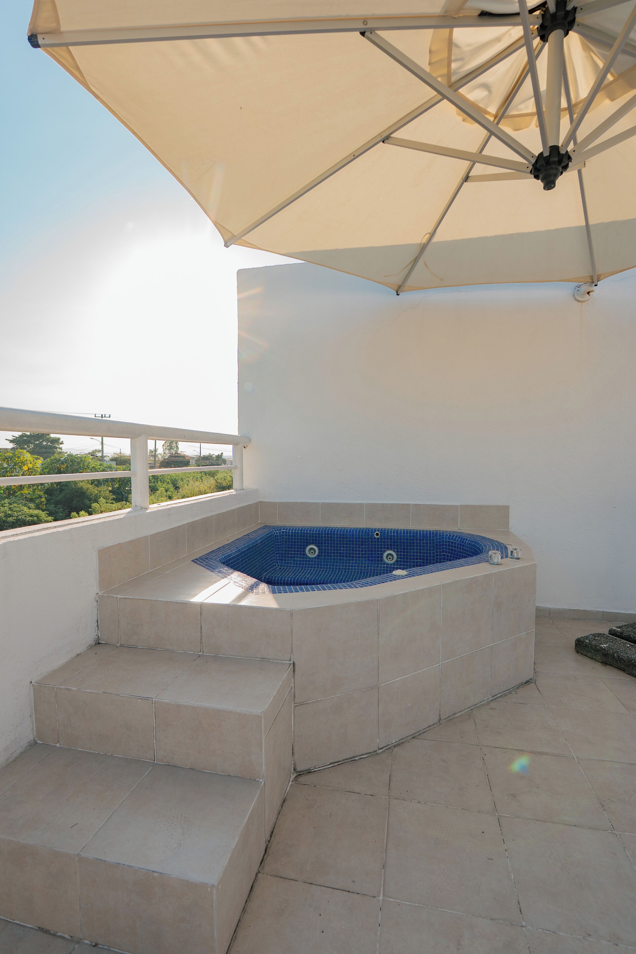 A hot tub with beige tiled steps leading up to it, under a large umbrella.