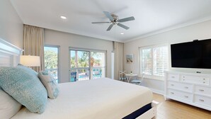 Ein Schlafzimmer mit einem großen Bett, einem Deckenventilator, einem Fernseher, einer Kommode und einem Balkon mit Blick.