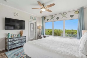 A bedroom with a large bed, a ceiling fan, a TV, a dresser, and a window with a view of greenery. - Exclusive Gulf View Condo with Pool Access (Miramar Beach)