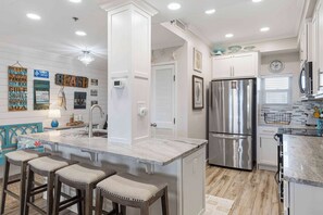 A modern kitchen with a central island, stainless steel appliances, and a decorative wall with nautical-themed signs. - Exclusive Gulf View Condo with Pool Access (Miramar Beach)