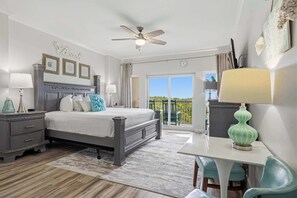 Une chambre à coucher comprenant un lit, des tables de chevet, un ventilateur de plafond, un balcon avec vue et un coin repas avec une table et des chaises.