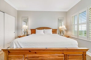 Ein Schlafzimmer mit einem hölzernen Bett, zwei Nachttischlampen, einem Nachttisch, einem Spiegel und einem Fenster mit Rollläden.
